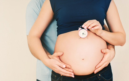 happy healthy pregnant woman with husband waiting baby with clock in studio の写真素材