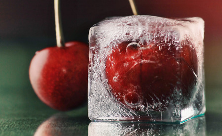 frozen delicious red cherry in ice  on green table with water drops macro backgroundの写真素材