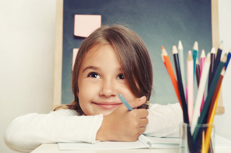 portrait of cute lovely girl drawing in copybook on blackboard background in classroomの写真素材