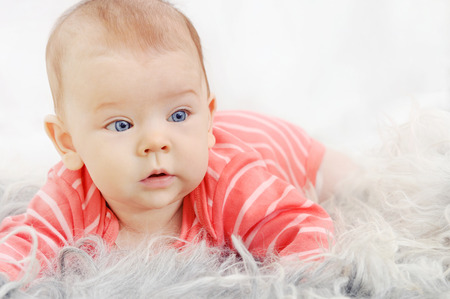 adorable cute little girl with big blue eyes and wide smile playing on the white sofaの写真素材