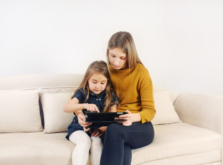 little girl with her mother using tablet device on the sofa at home, happy family, technology conceptの写真素材