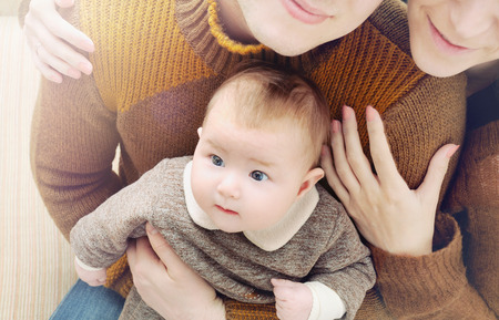 happy family of three, little cute baby with big eyes sitting on the parentの写真素材