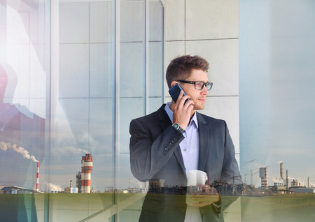 double exposure of urban attractive businessman with phone device and industrial enterprise building backgroundの写真素材