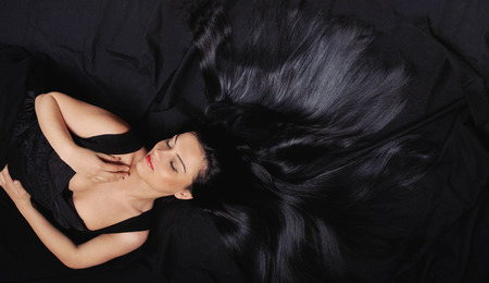 fashion chic woman with long bright black hair and silk shiny skin in studio on black backgroundの写真素材
