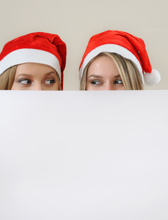 Tho happy girl in santa hat hiding behind a empty blank banner with copy space.の写真素材