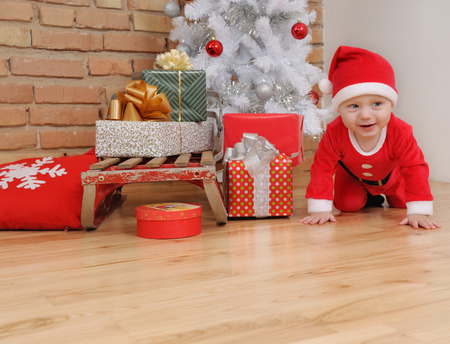 cute happy little baby boy in Santa suit and old vintage sled with gifts near Christmas tree.の写真素材