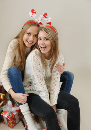 Two funny girls on the sled with gifts. Christmas and New Year concept. Studio shot on grey background. Christmas spiritの写真素材