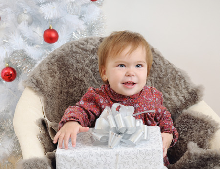cute little baby girl with big gift in hands near Christmas tree.の写真素材