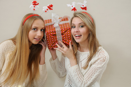 Two happy women hold near head and listen gift box.の写真素材