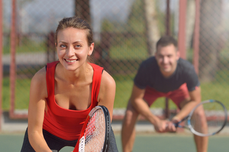 Couple playing doubles at the tennis court. Smiling woman at first plane. Healthy fitness concept with active lifestyle.の写真素材