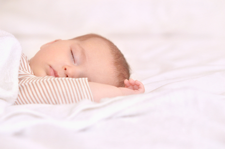 Peaceful baby lying on a bed while sleeping in a bright room. Newborn Sleep. Hands behind head. Happy motherhood conceptの写真素材