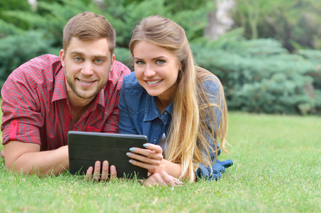 Happy couple lying in park using tablet pc together on a sunny dayの写真素材