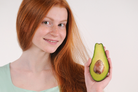 Beautiful smiling young girl posing with a half of avocadoの写真素材