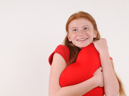 Young red hair girl tenderly hug a heart shape on grey backgroundの写真素材