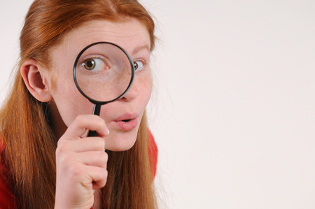 Portrait of a young red hair teen woman looking at the camera through a magnifying glassの写真素材