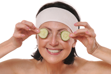 Cheerful mature woman holding pieces of cucumber in front of her eyesの写真素材