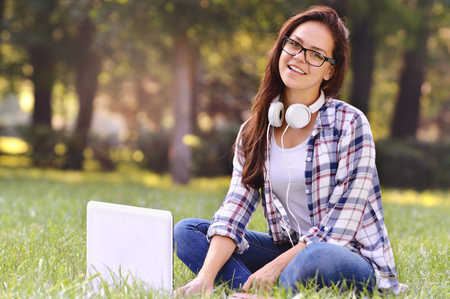 Student girl working on laptop, sitting on grass in parkの写真素材
