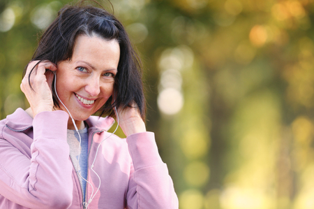 Portrait of elderly woman prepare to jog with headphones in the park in evening sunset. Attractive looking mature woman keeping fit and healthy.の写真素材