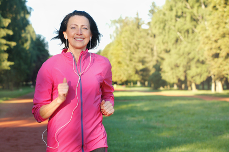 Portrait of elderly woman running with headphones in the park in early morning. Attractive looking mature woman keeping fit and healthy.の写真素材