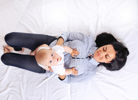 Portrait of beautiful mom playing with her baby in bedroom. Top view.の写真素材