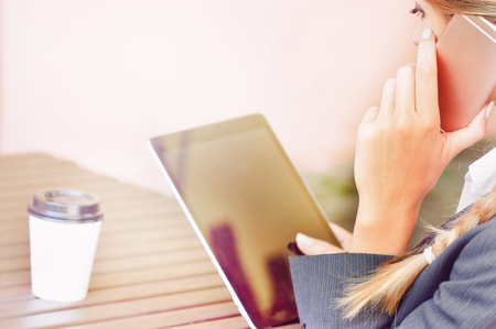 Young businesswoman working on digital tablet computer and talking by smart phone. Close up image of human hands holding a smartphone and using a tablet on the foregroundの写真素材