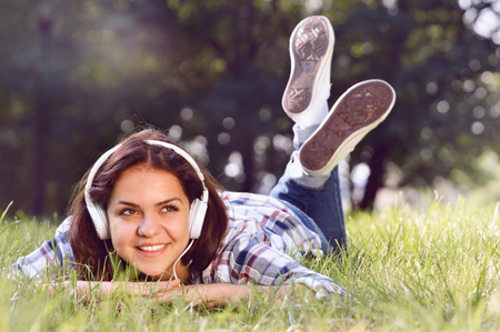 Close up portrait of Pretty young girl listening music lying at the grass. Cute teenage girl relaxing in parkの写真素材