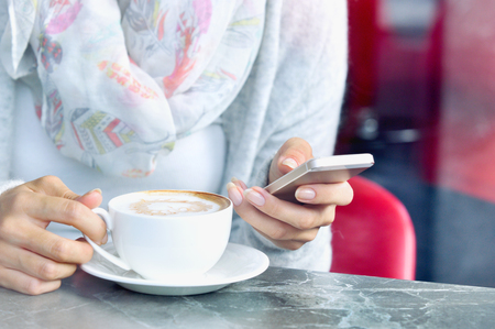 Close up view of coffee cup and hands of young women with smartphone at cafe. Lifestyle and technology conceptの写真素材