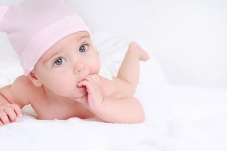 Cute baby lying on a white bedsheet and keeps fingers in his mouth. Happy childhood concept.の写真素材