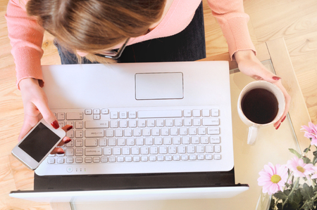 Woman working at the table. Top view of human hands, laptop keyboard, coffee,smartphone,sunglasses,notebook and a cacti on a wooden table backgroundの写真素材