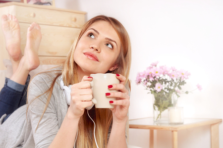 Happy woman with cup of coffee or tea lying at bedroom and dreaming about something goodの写真素材