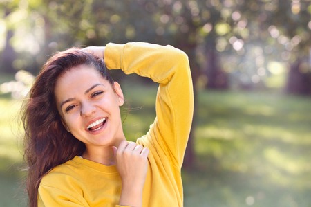 Young pretty girl in autumn or summer park. Happy young adult woman straighten one's hair and smilingの写真素材