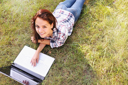 Student girl working on laptop, lying on grass in park. Student studying outdoors. Freelance job, online shopping, distance learning conceptの写真素材