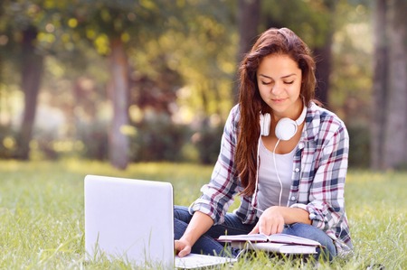Student girl working on laptop, sitting on grass in park. Student studying outdoors. Freelance job, online shopping, distance learning conceptの写真素材