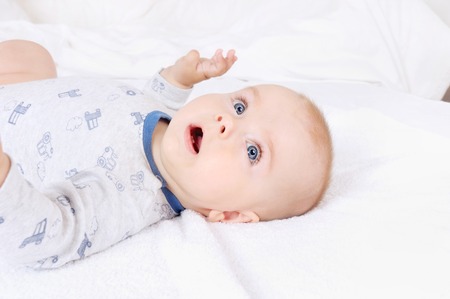 Funny baby infant child with blue eyes lying on the bed and looking at camera. Top view. Home, childhood and family concept.の写真素材