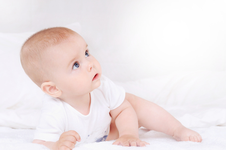 Portrait of little infant lies on a white bed in bedroom. Newborn child crawl in the bed. Nursery for young children. Textile and bedding for kidsの写真素材