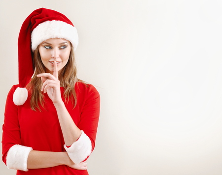 Christmas woman wearing a santa hat whispering christmas secret. Xmas concept. Empty space for greetings and adsの写真素材