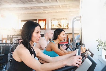 Group of three people in the gym, exercising their legs doing cardio training. Fitness young woman on gym bikeの写真素材