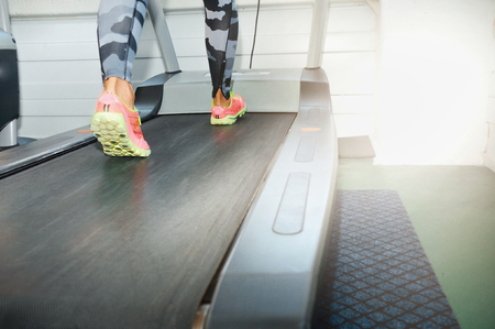 Close up of woman feet in colorful shoes running on treadmill machine in gym. Fitness center training. Healthy lifestyle concept.の写真素材
