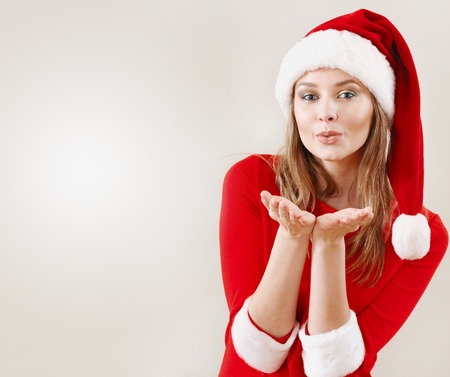 Christmas woman wearing a santa hat blowing a kiss. Xmas concept. Empty space for greetings and adsの写真素材