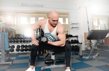 Very power athletic man bodybuilder do execute exercise with dumbbells on counter with dumbbells background. Fitness conceptの写真素材