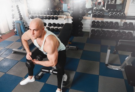 Strong athletic men pumping up muscles and train in gym workout. Bodybuilder man doing biceps exercise with dumbbell in fitness clubの写真素材