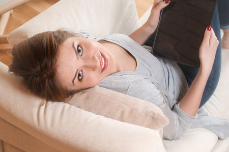 Beautiful woman at home working with a tablet. Woman in home cozy clothes sitting on a sofa using a tablet. View from above. Online education conceptの写真素材