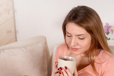 Young woman sitting on the sofa and drinking tea or coffee over the domestic background.の写真素材