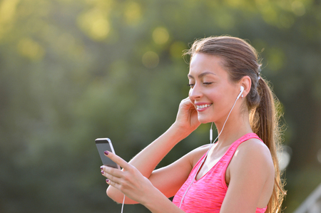 Portrait of fitness woman choosing music on her smartphone before or after jogging. Fitness girl training outdoorの写真素材