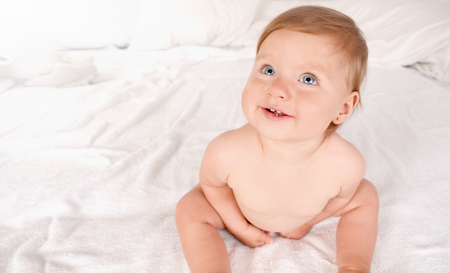 Happy newborn baby smiling and looking at camera. Top view. Happy smiling child with grey eyes on white bed background. Happy childhood conceptの写真素材