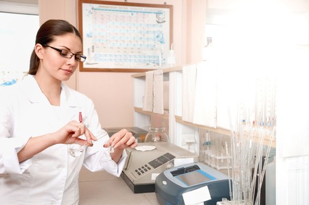 Female scientist researcher in white uniform is holding flasks while working in the laboratory. Discovering cure. Healthcare and biotechnology concept.の写真素材
