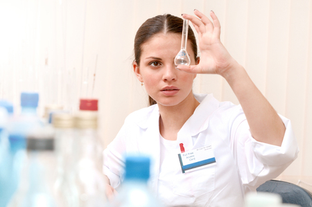 Beautiful young female scientist holding test tube and looking at it while working in the laboratory. Healthcare and biotechnology concept.の写真素材