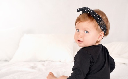 Cute baby girl dressed in a black dress on white bed background. Happy childhood conceptの写真素材