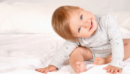 Happy newborn baby smiling and looking at camera. Happy smiling child with grey eyes on white bed background. Happy childhood conceptの写真素材
