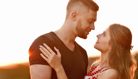Evening sun illuminates young couple hugging on field. Love, friendship and family conceptの写真素材